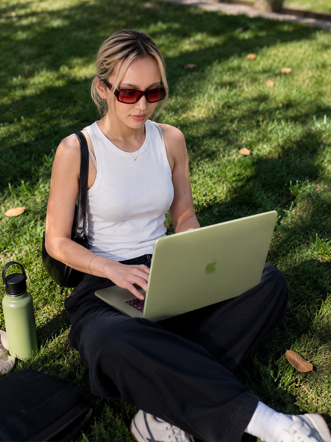 A creator filming in a sunlit park, green MacBook balanced on one knee