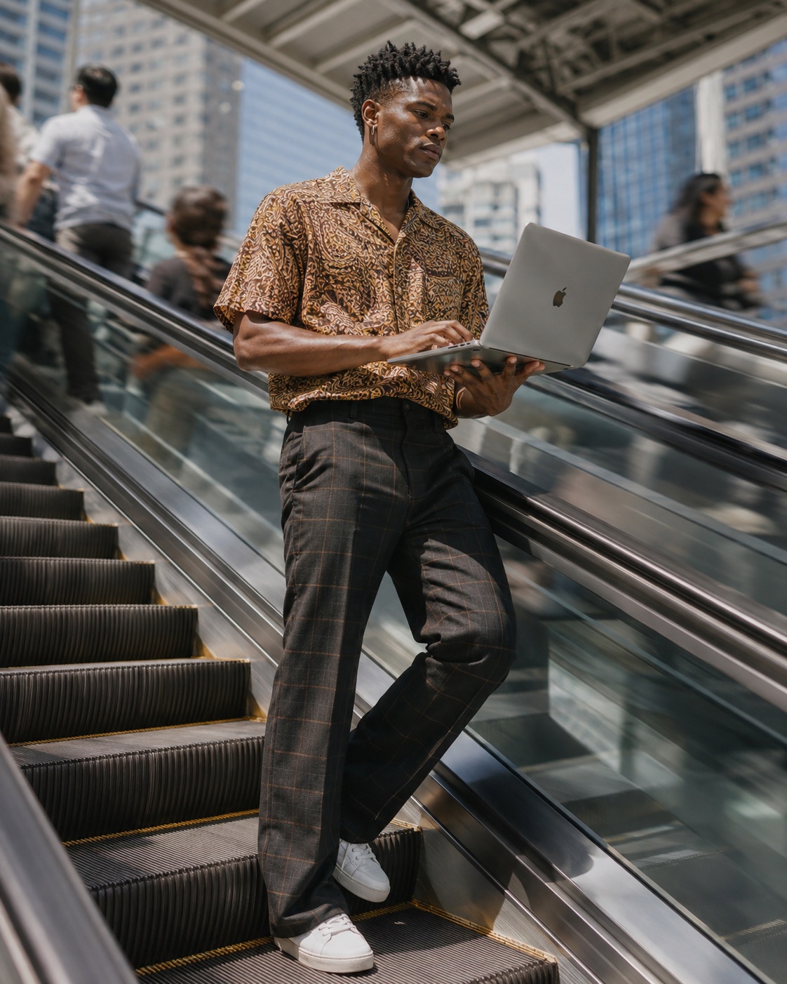 A man in a patterned shirt working on a MacBook while riding an escalator through a city walkway