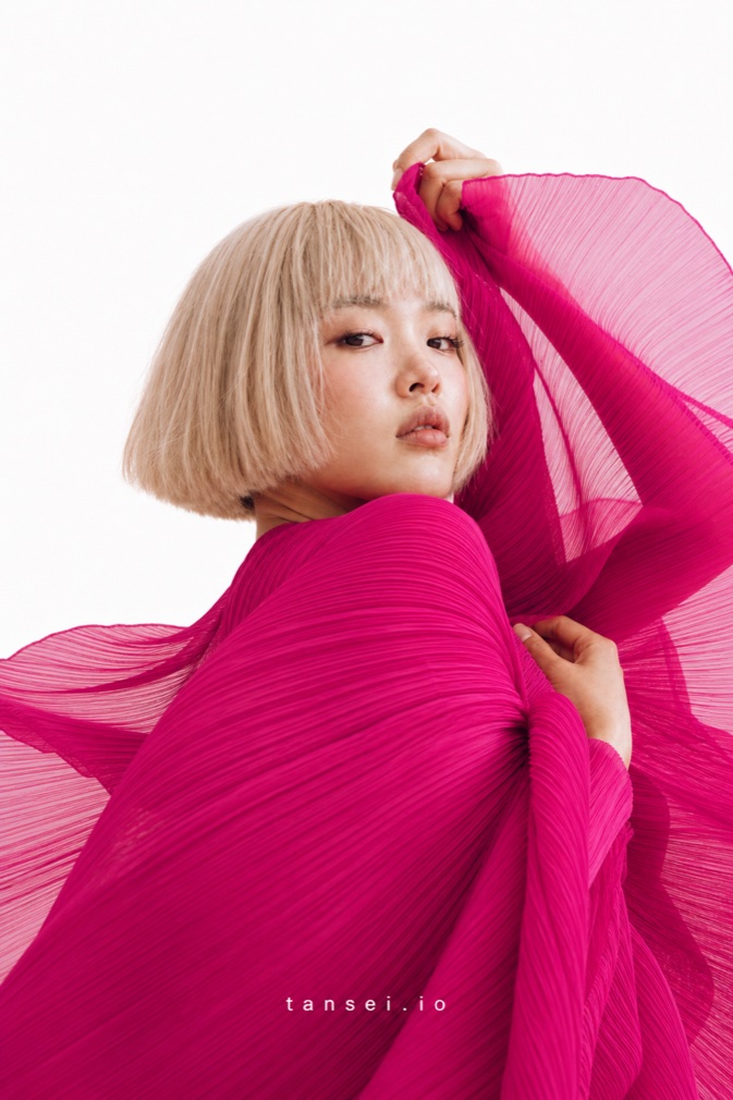 Tansei campaign photograph: model holding pink pleated fabric raised overhead